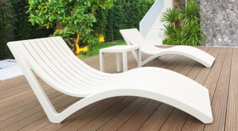 Chaise longue et mobilier de jardin modernes sur terrasse bois avec végétation luxuriante.