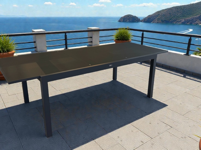 Table extensible Josephine en aluminium anthracite, idéale pour repas en extérieur avec vue imprenable sur la mer. Facile à agrandir de 180 à 240 cm pour accueillir plus de convives.