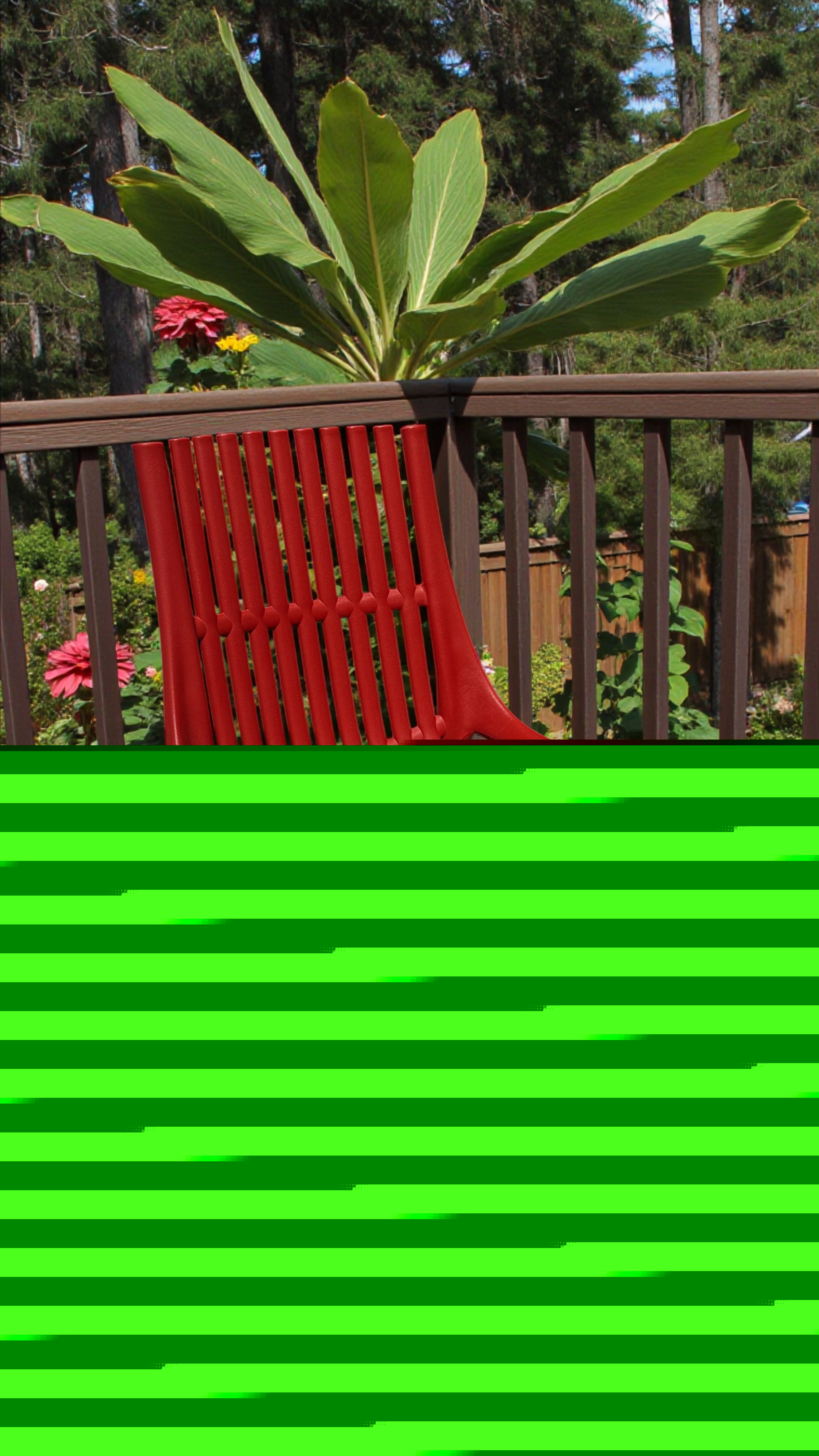 Chaise de jardin rouge en plastique avec lattes, idéale pour l'extérieur, sur une terrasse en bois avec un grand plant tropical en arrière-plan.