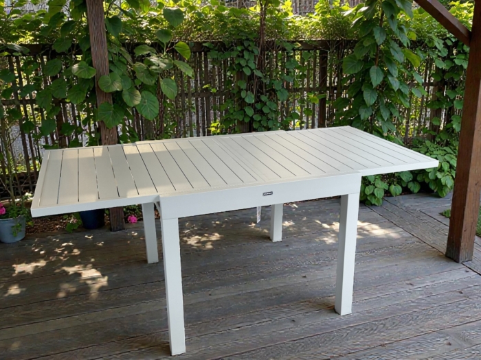 Table de repas extensible EOS 90 en aluminium beige, idéale pour les repas en extérieur, avec une extension de 90 à 180 cm, sur une terrasse en bois.