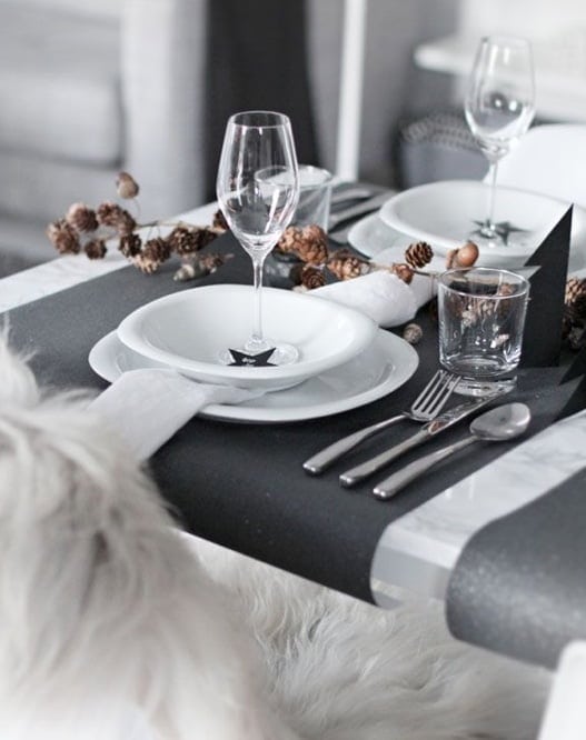 Assiette, verre à vin et table élégante pour dîner fin d'année ou événement spécial, décorée avec un chemin de table noir et éléments naturels. Ambiance sophistiquée et conviviale pour un week-end détente.