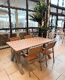 Un intérieur moderne avec une grande table en bois et des chaises en bois, éclairé par de grandes fenêtres laissant entrer la lumière naturelle, idéal pour un repas convivial en famille ou entre amis.
