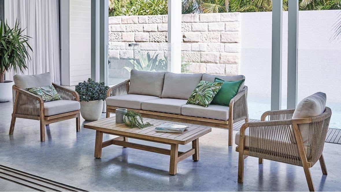 Fauteuils et canapé spacieux en rotin et coussins naturels dans une pièce lumineuse avec vue extérieure végétalisée.